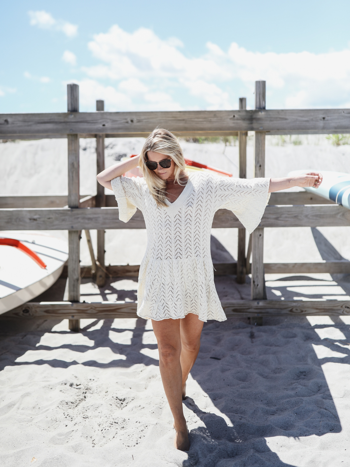 Woman standing on the beach in a cream knit dress with bell sleeves, sunlight highlighting the intricate chevron pattern.
