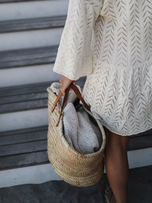 Close-up of a cream chevron-patterned knit dress with a woven beach bag, perfect for summer outings.