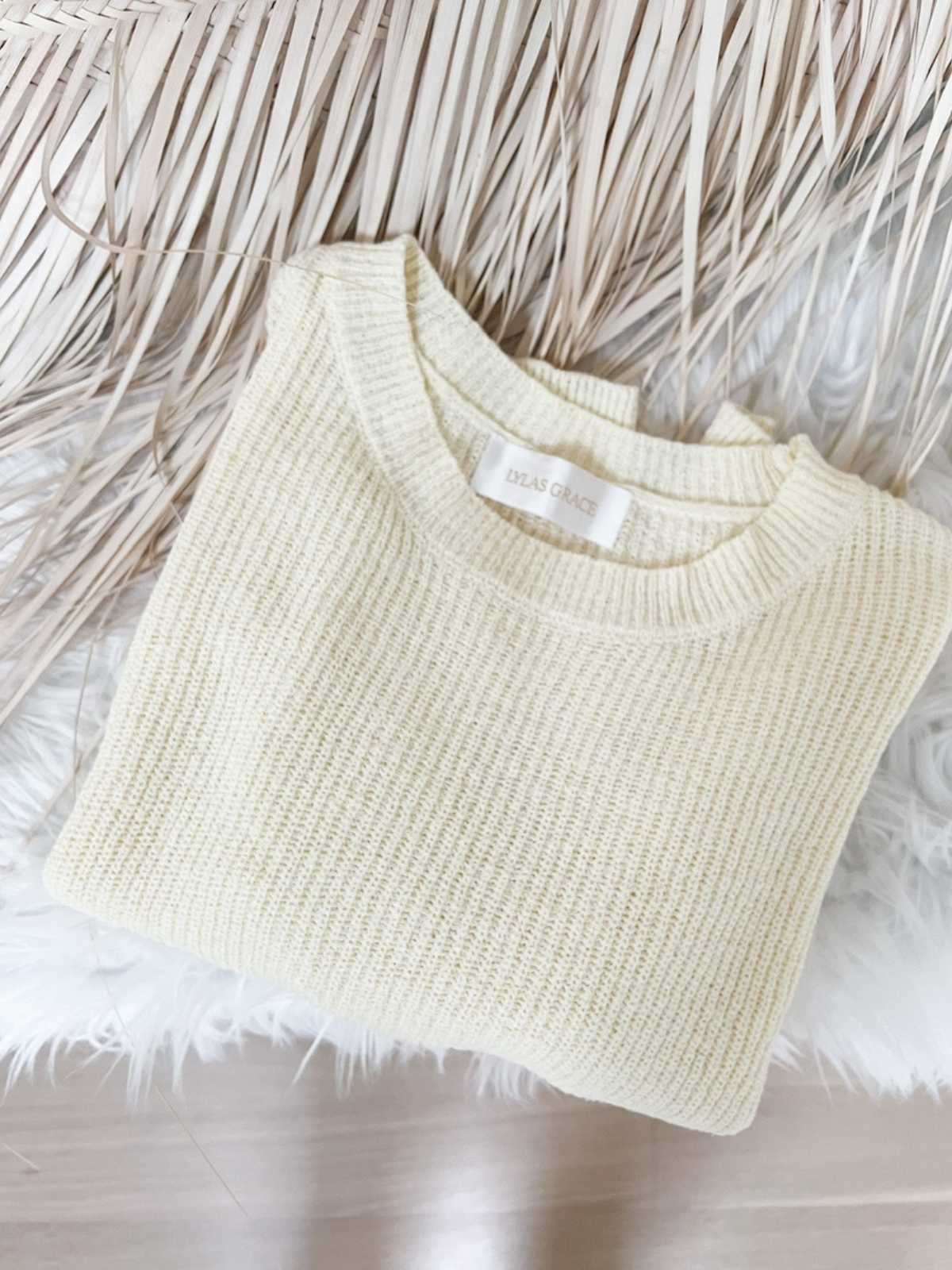 A neatly folded daffodil yellow sweater with a ribbed knit design, placed on a soft white fur background.