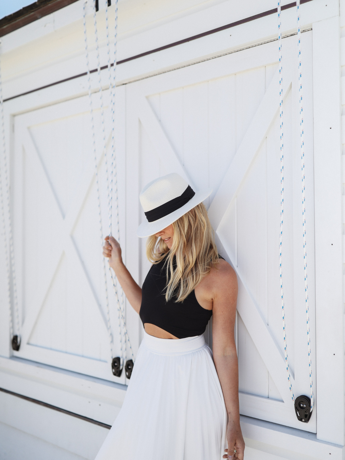 Woman leaning against a white wooden door, dressed in a black tank-style bodice and an elegant white skirt, accentuated with soft lighting.