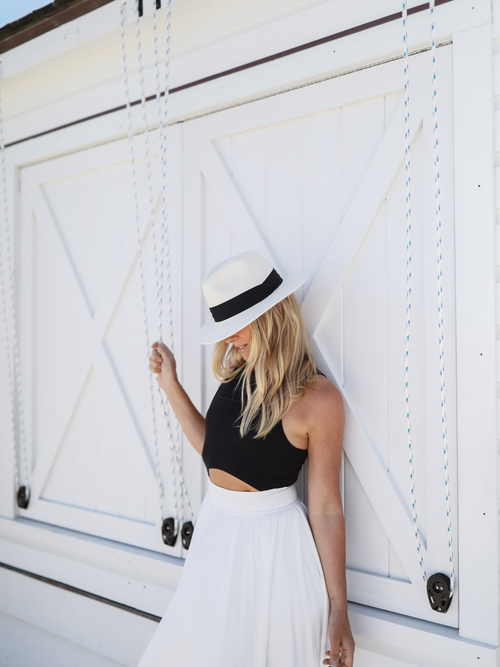 Woman leaning against a white wooden door, dressed in a black tank-style bodice and an elegant white skirt, accentuated with soft lighting.