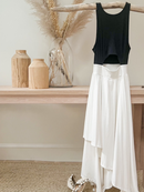 Black tank top and flowing white skirt displayed on a natural wood hanger, styled with neutral décor and pampas grass in a vase.
