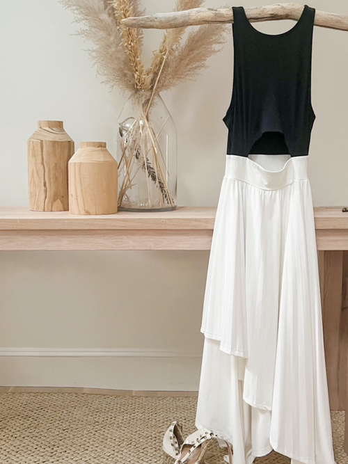 Black tank top and flowing white skirt displayed on a natural wood hanger, styled with neutral décor and pampas grass in a vase.